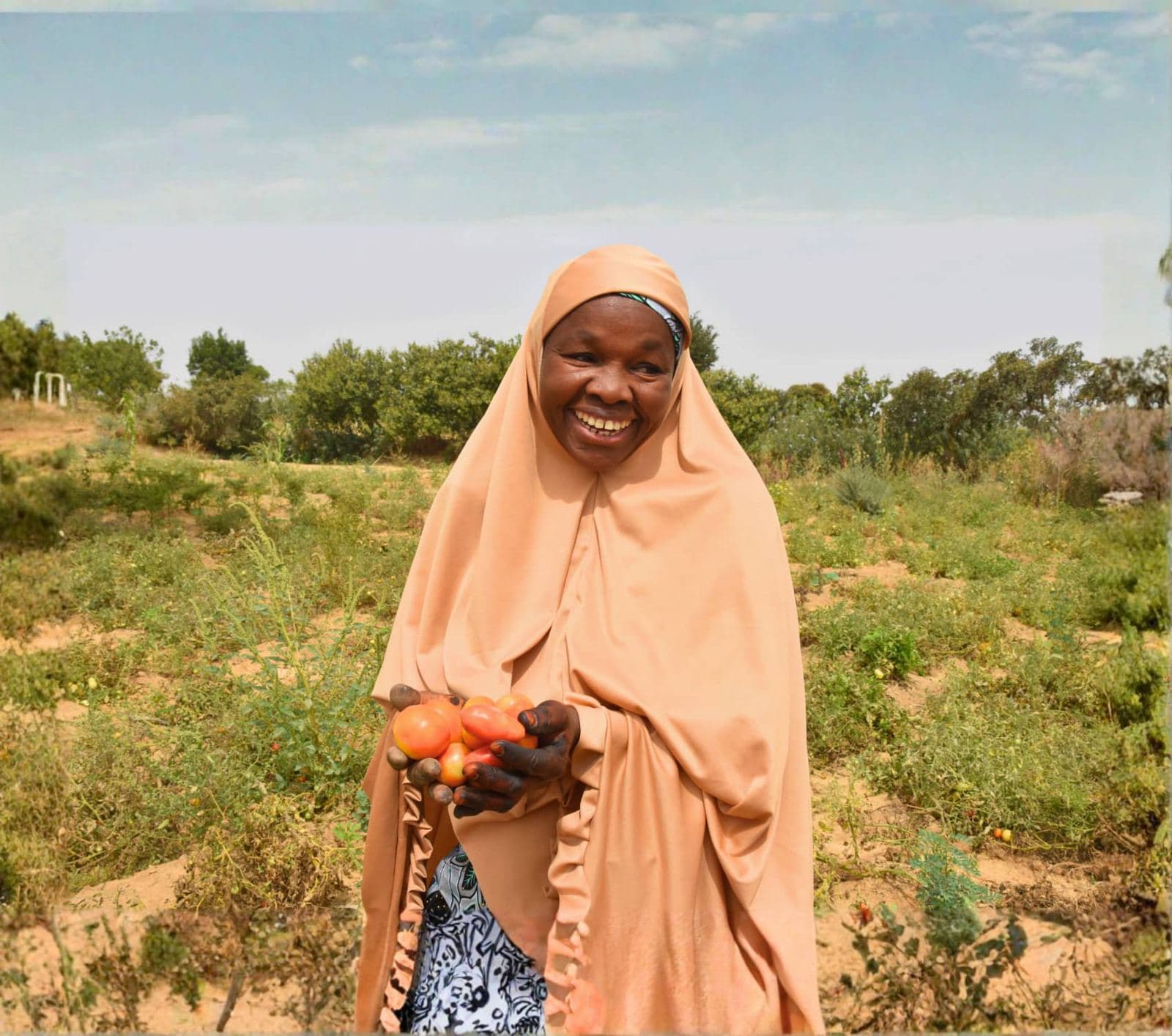 Smiling woman farmer holding fresh produce on her farm in Sokoto State