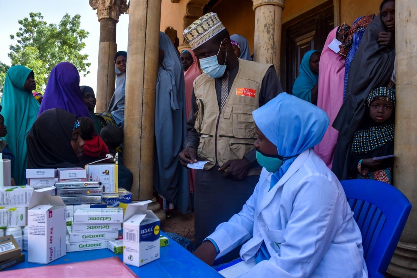 Health worker consulting with women and children at a health facility, with medicines on the table