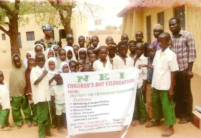 Pupils and teachers holding the NEI Children's Day Celebration banner, May 2011