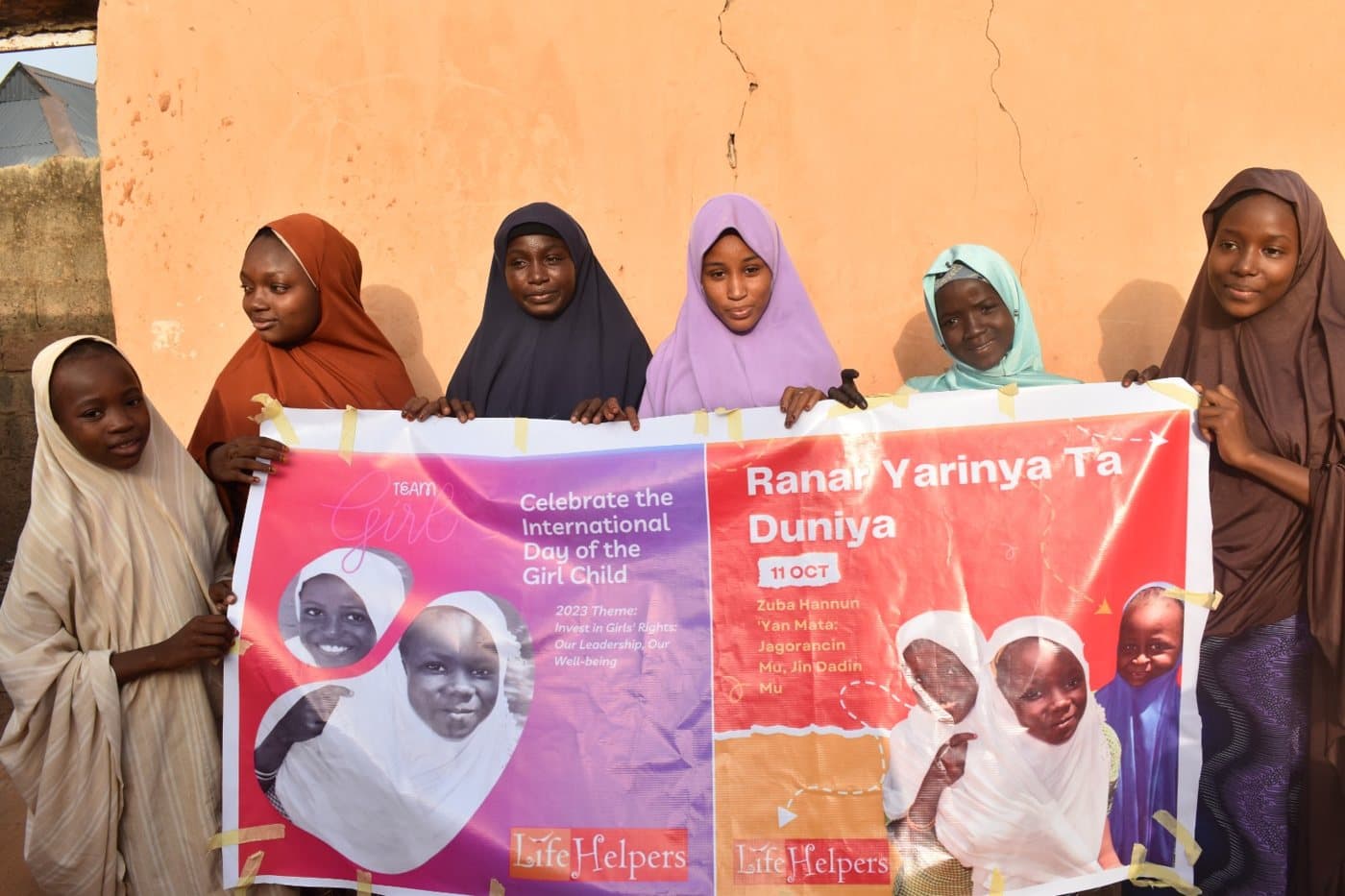 Girls and women holding a “Ranar Yarinya Ta Duniya” International Day of the Girl Child banner
