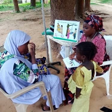 Health worker using a picture chart to talk to a mother and her daughter about immunisation