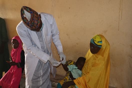 Health worker immunising a child held by her mother during outreach